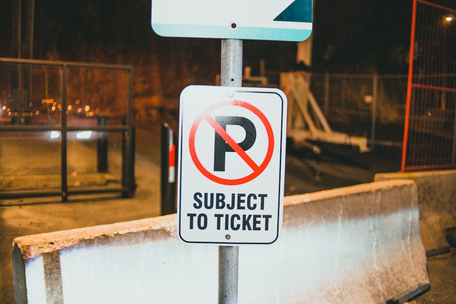 A fallen rectangular metal street closure sign with a white background and black lettering reading 'STREET CLOSED' lies on a paved sidewalk next to a small dirt area with wooden edging, which contains some soil and a few small plants. The sign is attached to a metal frame with two supports, one of which is partially visible. Several people's footwear, including sneakers and boots, are seen standing nearby on the pavement. The scene appears to be in an urban area with tiled pavement, and the fallen sign indicates temporary street closure, possibly related to local regulations or work permit enforcement, as suggested by the webpage about street-closure rules and potential fines. The image is relevant to house removals and moving logistics, illustrating the importance of coordination and awareness of street restrictions during home relocation activities, with [COMPANY_NAME], Man with Van Elmstead, operating within the context of removals.